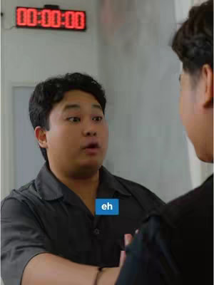 The cover image shows two men in a room. The primary focus is on the man in the foreground, who is looking shocked or surprised, his mouth slightly open. The background features a digital clock displaying "00:00:00". There is a blue rectangle at the bottom of the image that says "eh".