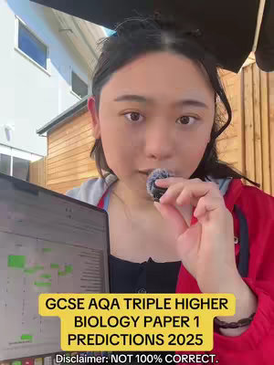 A young woman is holding a microphone next to her face while looking at a laptop screen. The screen has information that appears to be school-related. Overlay text at the bottom announces GCSE AQA triple higher biology paper 1 predictions for 2025. The backdrop is an outdoor setting with trees, a partial view of a house, and an umbrella.