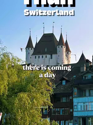 The cover image showcases Thun Castle in Switzerland, set against a bright blue sky. Above the castle, the word 'THUN' is written in large, bold white letters with a black outline. The text 'Switzerland' appears beneath it, also in white. Below the castle, the phrase 'there is coming a day' is written in large white letters. The bottom of the image shows the green foliage of a tree and a portion of buildings.