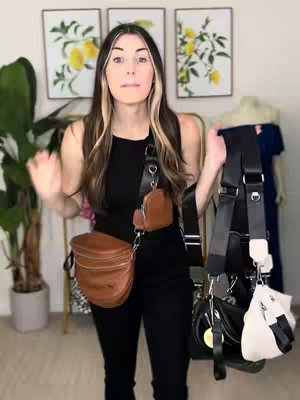 A woman stands facing the camera, holding several bags. She appears to be in a well-lit room. Behind her are framed pictures and a tall plant.
