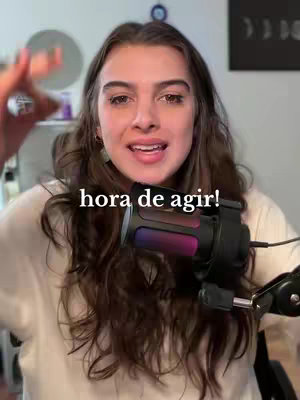 A woman with long brown hair is speaking while holding a microphone. The background is a blurred room, and the text overlay says 'hora de agir!' in bold, black font.