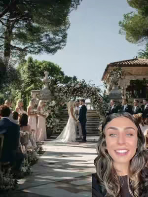 A woman smiles in the bottom corner with a wedding scene in the background. The wedding is outdoors with the couple under a flower arch. Bridesmaids and guests are on either side of a stone staircase. The scene is bright and sunny, and mostly green and stone colors.