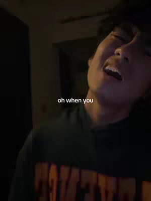 A man with dark hair and closed eyes is captured mid-scream, his mouth wide open. He wears a green and orange sweater with an unclear design. Simple white text appears on the image, with dark shadows in the background.