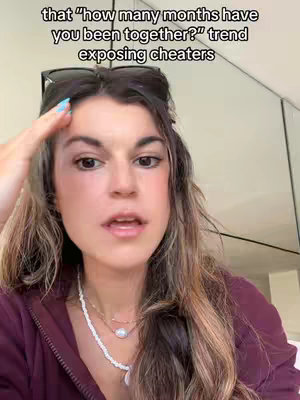 A woman with medium-length brown hair, wearing a purple zip-up jacket over a white top, and a necklace. She has sunglasses perched on her head, showing her hand on her head with a thoughtful expression. Text overlayed at the top says the video addresses a trend about exposing cheaters.