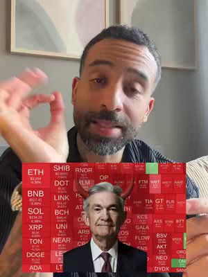 A man with a beard makes an "okay" sign in front of a split screen. The top half shows the man in a black shirt indoors, while the bottom half shows a red background with a chart of various cryptocurrency symbols and logos such as ETH, SHIB, BNB, and XRP. In the center of the chart is a picture of Jerome Powell with devil horns.