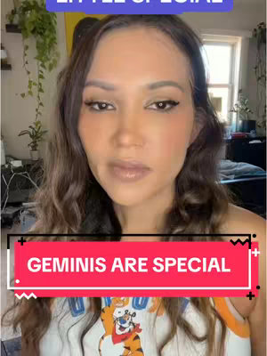 A woman with long, wavy brown hair is centered in the frame. She appears to be in her late 20s to early 30s, has a medium skin tone, and is wearing light makeup. The background shows glimpses of a room with plants.
