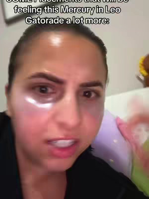 A close-up shot of a woman with fair skin, looking directly at the camera. Her face is slightly flushed, and she appears unwell. She has dark eyebrows and dark hair pulled back off her face. She has eye patches on, the skin around her eyes appears slightly red. Behind her is a pillow and part of a wall.
