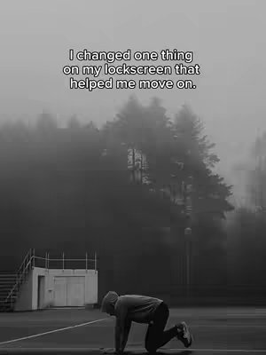 A black and white image depicts a person on their hands and knees on a wet surface, possibly a track. The background is blurred, consisting of a line of trees shrouded in fog. The sky is grayish-white suggesting overcast weather. Text overlayed in the top of the frame.