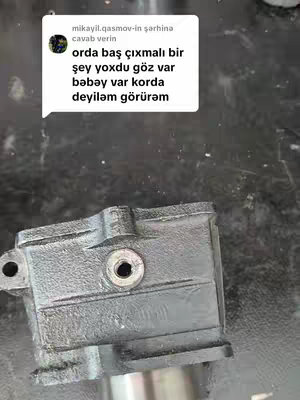 The image presents a close-up shot of a metallic component, likely a part of a mechanical system. The component is dark in color, with areas of black and hints of silver where the surface is worn. There's a circular opening and other geometric shapes. Overlaying the object is a white speech bubble, containing text in an unfamiliar language.