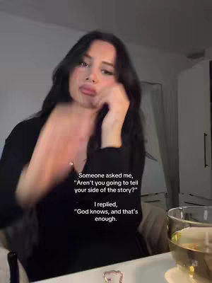 A woman with long dark hair is the main focus, slightly offset in a close-up shot. She is positioned indoors, with soft lighting, suggesting a relaxed setting. She is wearing a black long-sleeved shirt. A glass with liquid is partially visible to the right. Text overlays the image, written in a clear, white font.
