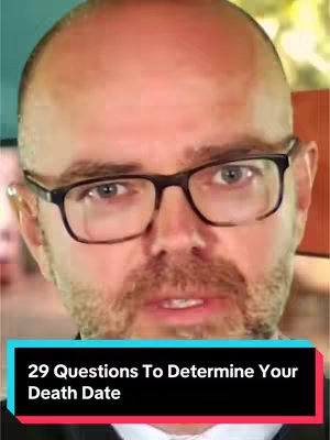 A man wearing glasses is centered in a close-up shot. He has a bald head and a goatee and is looking directly at the camera. The background is a blur of warm tones.