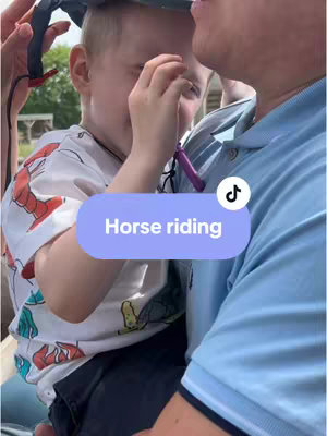 A light blue, rounded rectangle with the text "Horse riding" in white is overlaid on the bottom-middle of the image. The background is outdoors, with a young child being held by an adult. The child is wearing a shirt with colorful graphics, and the adult is wearing a light blue polo. The TikTok logo is visible on the top of the rounded rectangle. The focus is on an emotional moment between the child and the adult.