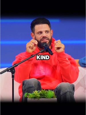 The cover image shows a man with a beard, wearing a red hoodie. He's seated and speaking into a microphone, fingers raised. Overlayed on the image is a text box with the word 'KIND'. The background is blurred with a stage look.