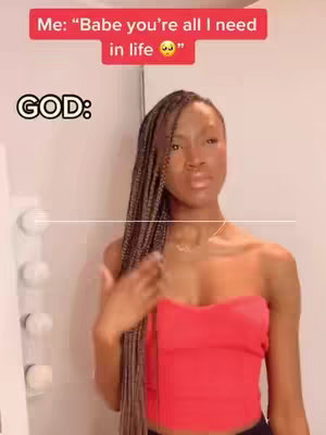 A woman with long, braided hair, wearing a red strapless top, poses in front of what looks like a white door. Text overlays appear in the image: a red bar at the top with white text, and the word 'GOD:' in bold white letters.