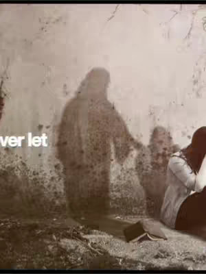 The image is composed with a sepia-toned color palette. A blurred background features a grunge-style wall texture with a vague, figure-like shadow dominating the left side. In the foreground, there is a person sitting on the ground facing away from the viewer, possibly in a moment of reflection or prayer, their head bowed and the hand on their face. A light-colored top and dark bottom can be seen in the close up shot. In front of the person, there is an open book suggesting a religious context, with a shadowy figure of a person standing and gesturing. Both figures may be representing Jesus and a follower. The overall composition evokes a sense of spiritual reflection.