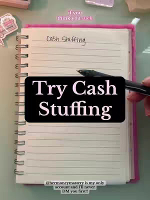A notebook with lined paper is open to a double-page spread. The left page bears the handwritten title 'Cash Stuffing'. A large black rectangle featuring the words 'Try Cash Stuffing' in white text overlays the lower portion of the pages. A pen is held near the text. Surrounding the notebook are office supplies.