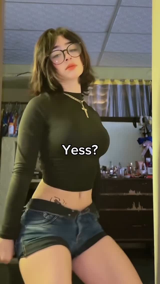 The cover image is a selfie of a woman in a room, posing. She is wearing glasses, a black long-sleeve top, and short denim shorts. She is wearing a necklace with a cross. The text overlay at the bottom says, 'Yess?'