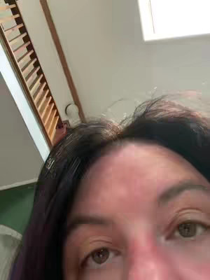 A close-up shot features the upper portion of a person's face, with dark hair framing the forehead and eyes. The lighting appears soft, and the background includes a staircase.