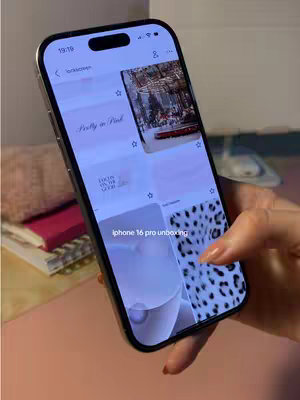 A close-up shot shows a hand holding a black iPhone, displaying the lock screen. The phone is angled slightly, and the hand holding it is in the lower right corner. On the screen, a Pinterest-style interface is visible, with different screensaver options displayed.