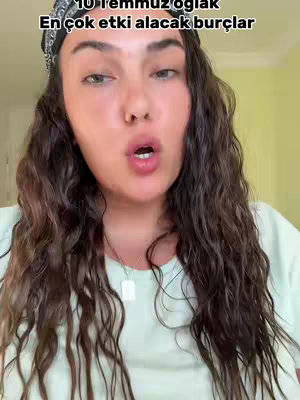 A woman with long, wavy dark hair is centered in the frame, looking directly at the camera with her mouth open. She wears a bandana and a light-colored t-shirt, with a necklace. Text overlay indicates her content is about astrological signs.