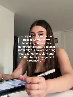 A young woman is seated at a desk, looking at a laptop and holding a pen. Text overlayed on the image includes text about studying and breaking generational curses.