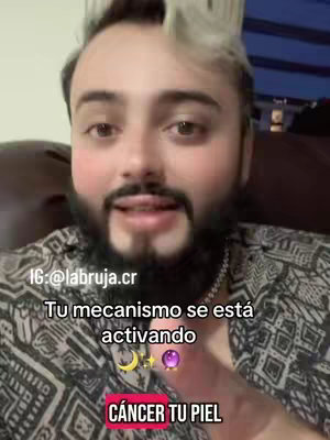 The cover image is a selfie-style video shot featuring a man with a beard and light-colored hair. He is wearing a patterned shirt and a silver chain. Text overlays are present, including a user handle and phrases in Spanish like, "Tu mecanismo se está activando" and "Cáncer Tu Piel." The background appears to be an interior space, likely a home, with a subtle play of light and shadow.