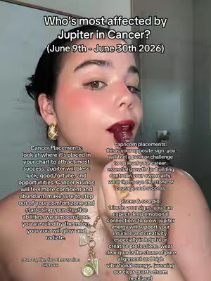 A woman with dark hair, blush, and red lipstick is holding a lipstick tube up to her lips. Text overlays the image, with additional astrological information. The background is a bathroom setting, suggesting a mirror.