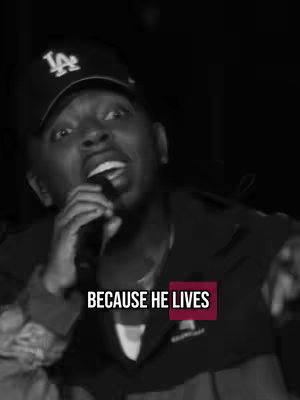 A black and white image showing a man with a LA Dodgers cap speaking into microphone. The text overlay 'BECAUSE HE LIVES' appears onscreen.