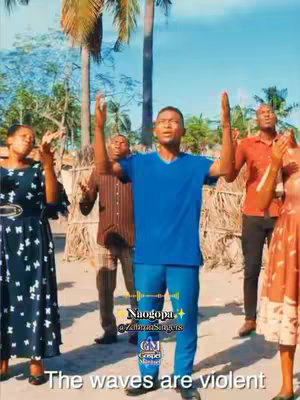 The cover image shows a group of African people in an outdoor setting with a bright blue sky. A man in a blue shirt and pants is in the middle with his arms raised towards the sky; he looks to be singing or speaking. Other people are positioned around the man, most with their hands raised as well. The background includes trees and a small structure. Overlayed text is displayed on the image with the title of the song/video. The image uses a vertical layout.