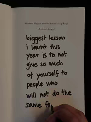 A notebook page with handwritten text in black ink, with a hand writing on the bottom right corner.