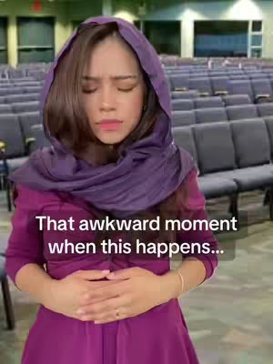 A woman in a purple head covering and dress is in a church setting. Her arms are crossed over her abdomen, and her eyes are closed, suggesting prayer or introspection.