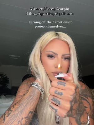 A woman with long blonde hair holds a lighter to her mouth, with text overlayed. She has tattoos on her arms.