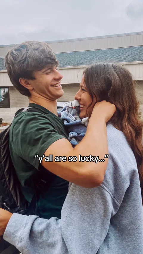 A couple laughing and embracing, with the man in a green shirt and the woman in a gray sweatshirt. A blurred background suggests an outdoor setting. Text overlay is visible.
