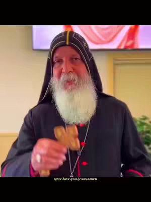 The cover image features a close-up shot of a religious figure, likely a bishop or priest, holding a wooden cross. He has a white beard and is wearing a dark, hooded robe with a black and gold headdress. The background is neutral, with a hint of an image on a screen behind him and a few blurred green plants to the right.