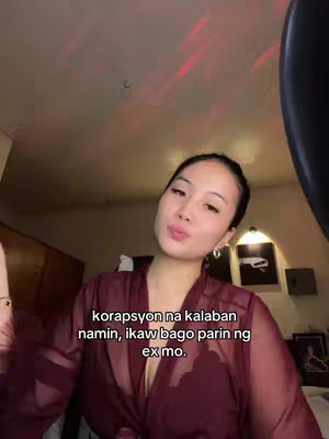 A woman in a maroon robe is positioned with a slightly elevated camera angle in her room.  The lighting is a mix of warm, artificial lights, producing red highlights on the ceiling.  The room's interior has simple furnishings in the background.