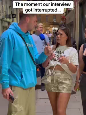 The cover image shows a man in a blue hoodie interviewing a woman in a white t-shirt and camouflage shorts on a city street at night. Another man with a microphone is visible in the background. The overall composition is a medium shot focusing on the two main subjects.
