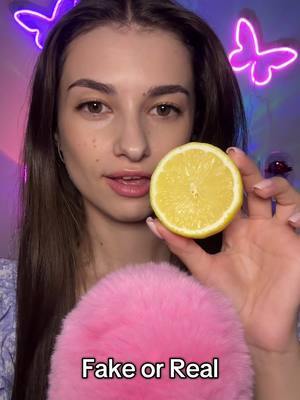 A woman with long brown hair is holding a halved lemon and a pink fluffy object. The background features two neon butterfly lights.