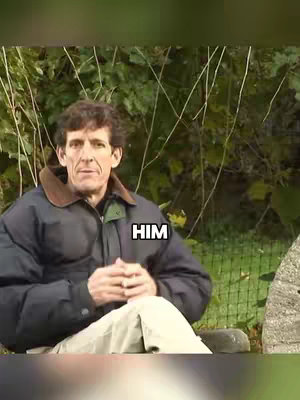 A man with short brown hair wearing a dark blue jacket with a brown collar sits on a stone bench in front of a backdrop of green foliage. An overlay of the word "HIM" is placed over his jacket.