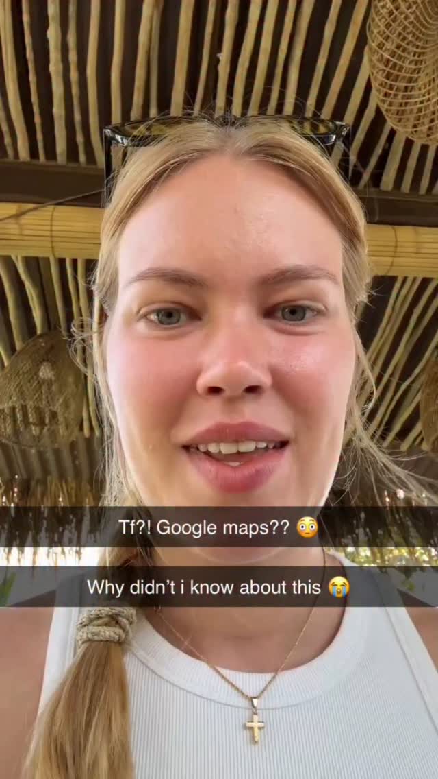 A selfie-style video cover image features a light-skinned woman with blonde hair, looking directly at the camera with an open mouth in apparent surprise. Two lines of overlaid white text appear near the bottom, with the first querying 'Tf?! Google maps??' and the second, 'Why didn't i know about this', complete with a crying emoji, reinforcing the expression of surprise and disbelief. The background includes bamboo and woven textures.