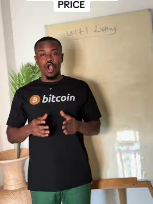 A man in a black Bitcoin t-shirt stands in front of a whiteboard with "WIFI Listing" written on it. He is mid-sentence with an open mouth and gesturing with his hands.