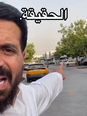 A man with a beard is pointing to the right, off-camera. Above his head is text in a stylized Arabic font. In the background is a street scene with cars, trees and buildings.