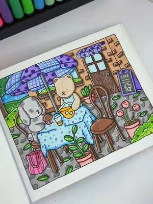 A colorful illustration of a cafe scene with cartoon characters. A bear wearing a blue apron is pouring something into a yellow bowl, a bunny sits across the table, and a cupcake and drink sit on the table. There's a blue-and-purple polka-dotted umbrella, and the background shows a brick building with a door and a cafe sign reading 'CAFE'.