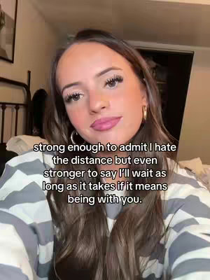 A young woman with long brown hair and a striped sweater is centered in the frame. Text overlays are present. The background is softly lit with warm tones, indicating a possibly indoor environment.