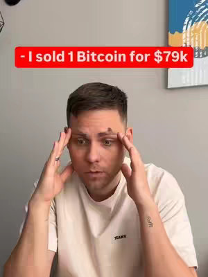 A man with short brown hair, white t-shirt with the word `TEANT` on it, and a mole on his forehead looks stressed and confused with his hands on his head against a light background.