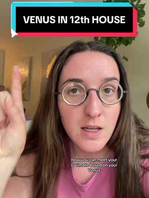 A woman with long brown hair and round glasses looks directly at the camera, pointing her right index finger upwards. Above her head, a banner reads 'VENUS IN 12th HOUSE'. Below her, text mentions meeting a soulmate based on Venus. The background is softly lit, featuring hints of foliage and a light-colored wall.