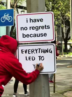 A person in a red hoodie is writing on a white sign. The sign is on the pillar. There are two signs, one above the other