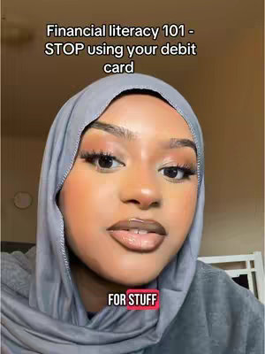 The cover image features a close-up shot of a woman with a hijab, facing the camera. The woman has a neutral expression, and the focus is on her face, with her eyes and lips clearly visible. The background is a blurry indoor setting, and text overlays at the top and bottom provide context, indicating a financial literacy topic.