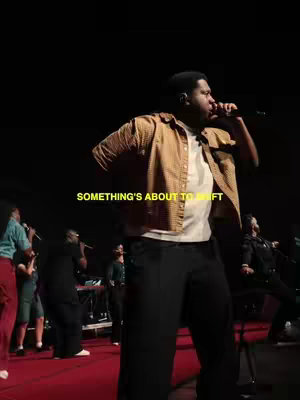 A live music performance stage with a man singing into a microphone, surrounded by other musicians and a red-lit floor and dark background. Hook text across the image.