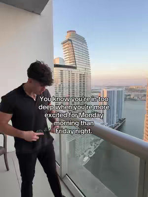 A man stands on a balcony, overlooking a city skyline with a tall building and water. He wears a black shirt and pants, holding sunglasses. Text overlays offer motivational messages.