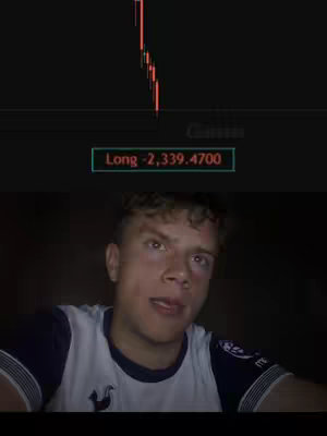 The cover image displays a split of a stock chart and a person. The top portion shows a black background with a red and green line graph indicating stock value changes. Beneath the graph, a text box reads 'Long -2,339.4700'. The lower half features a young man, appearing to be recording on camera. He is wearing a white and navy soccer jersey, has light skin with brown eyes and is angled slightly, with a neutral expression.